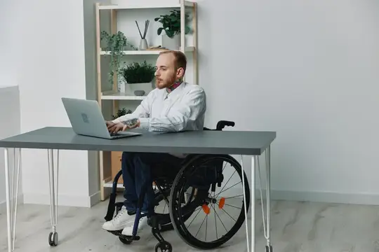 Мужчина в инвалидном кресле работает за ноутбуком в светлом офисе