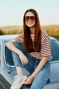 Улыбающаяся девушка в солнечных очках сидит на капоте ретро-автомобиля
