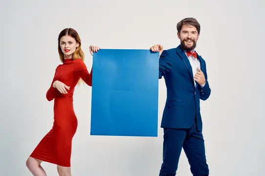 Мужчина в синем костюме и женщина в красном платье держат синий лист