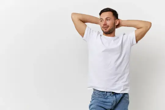 Молодой, сексуальный, счастливый, загорелый, симпатичный мужчина в базовой футболке со сложенными за головой руками позирует изолированно на белом студийном фоне