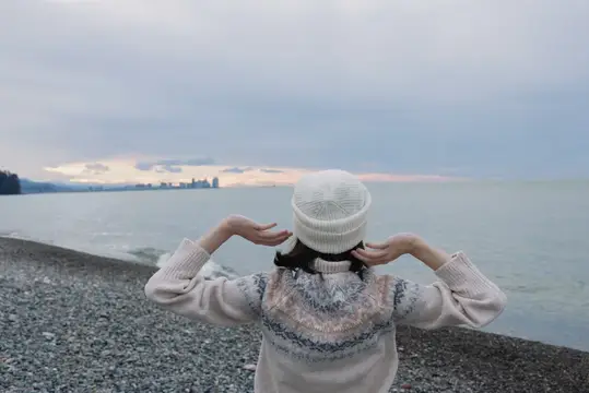 Девушка в белой шапке смотрит на закат у моря