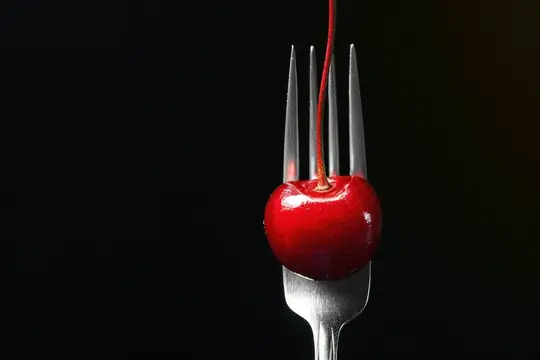 Спелая вишня на зубцах вилки на чёрном фоне