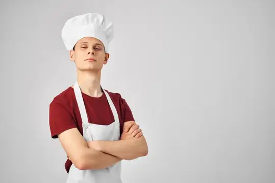 Молодой повар в колпаке и фартуке стоит со скрещёнными руками
