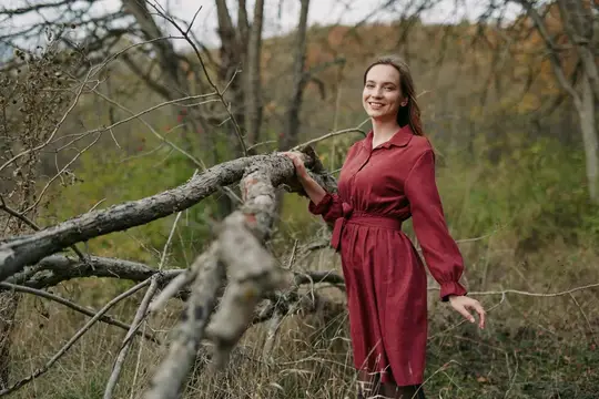 Улыбающаяся девушка в бордовом платье у поваленного дерева