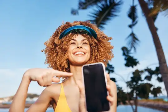 Улыбающаяся кудрявая девушка в козырьке показывает на смартфон