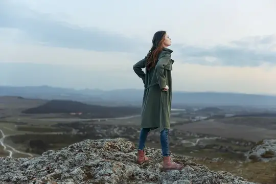 Женщина любуется захватывающей панорамой с вершины горы, на заднем плане виднеются долина и горы