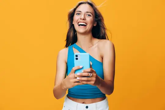 Красивая молодая женщина улыбается и держит смартфон на ярком оранжевом фоне