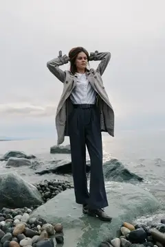 Молодая женщина в плаще стоит на камне у моря
