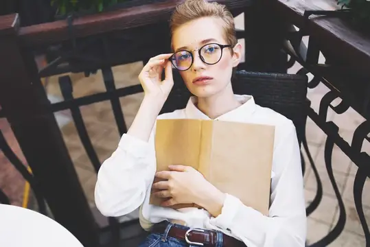 Молодая женщина в очках с книгой у чугунной решётки