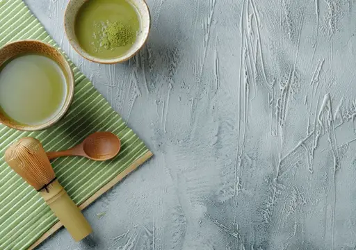 Привлекательная композиция для маття с чашами зеленого чая, бамбуковым венчиком и текстурированной серой поверхностью