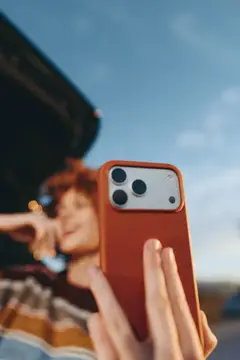 Рыжеволосая девушка фотографирует на смартфон в оранжевом чехле