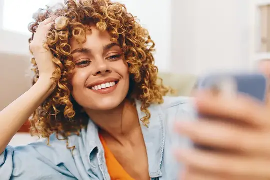 Кудрявая девушка улыбается, делая селфи на смартфон