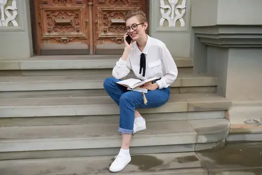 Симпатичная женщина в очках гуляет по городу с книгой, олицетворяя образование