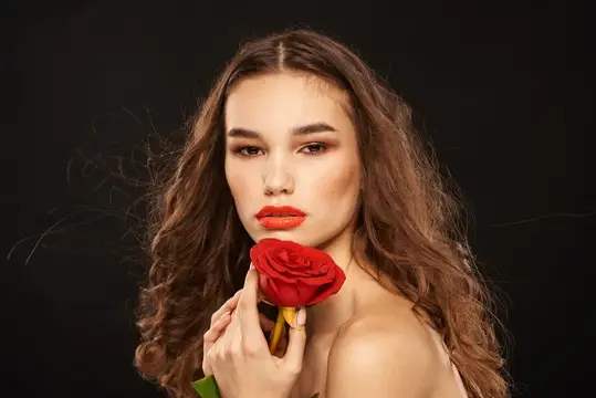 Молодая женщина с красной розой у лица на чёрном фоне