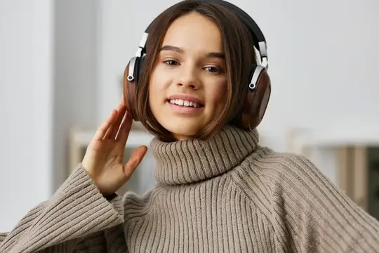 Улыбающаяся девушка в наушниках слушает музыку дома