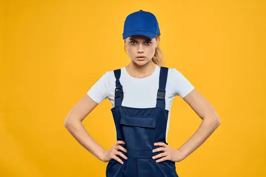 Женщина в рабочей униформе и синей кепке, оказывающая курьерские услуги, желтый фон