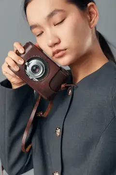 Азиатская девушка с закрытыми глазами держит винтажный фотоаппарат в кожаном чехле