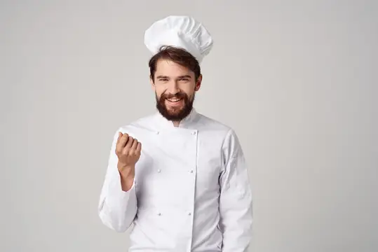 Улыбающийся бородатый повар в белом колпаке на сером фоне