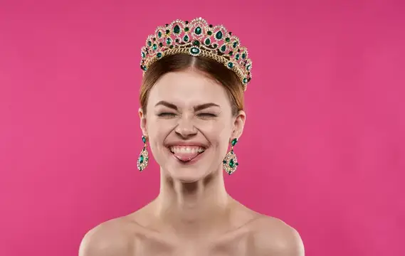 Эмоциональная женщина на розовом фоне, сморщенное лицо и диадема, крупный план портрета