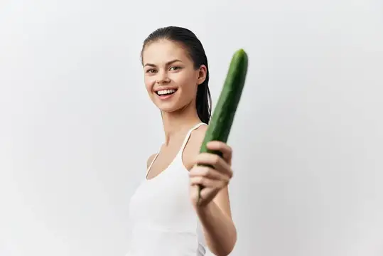 Игривая молодая женщина весело держит огурец с яркой улыбкой