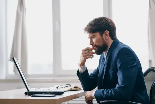 Мужчина сидит перед ноутбуком в офисе, перед ним открыт ноутбук, он выглядит как руководитель или менеджер