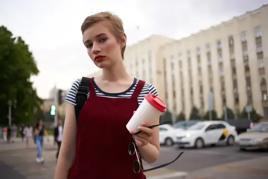 Молодая женщина с кофе на фоне городской улицы