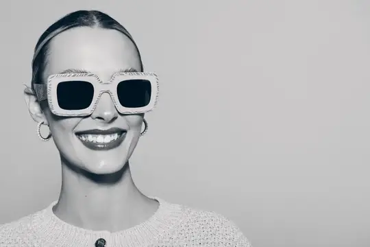 Улыбающаяся девушка в больших солнцезащитных очках на сером фоне