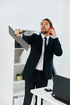 Удивлённый мужчина в костюме с папкой говорит по красному телефону