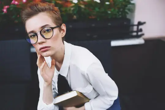 Рыжеволосая девушка в очках с книгой задумчиво смотрит в сторону
