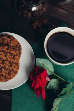 Чашка черного кофе с печеньем и красной розой на зеленой салфетке