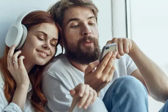 Рыжеволосая девушка в наушниках и бородатый мужчина со смартфоном