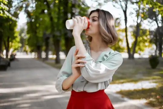 Молодая женщина пьёт воду из бутылки в летнем парке