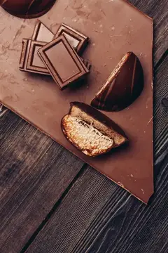 Кусочки молочного шоколада и конфета с ореховой начинкой на деревянном столе