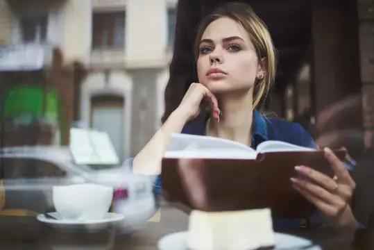 Задумчивая блондинка с книгой у окна кафе