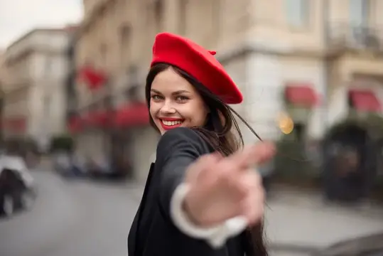 Модная женщина улыбается, показывая зубы, стоя на улице на фоне города