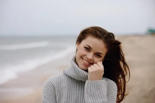 Весёлая женщина с длинными волосами гуляет по пляжу, наслаждаясь природным пейзажем
