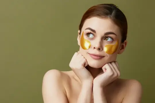 Молодая женщина с золотыми патчами под глазами мечтательно улыбается