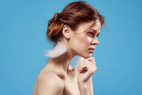 Женщина с обнаженными плечами, модные украшения, серьги на голубом фоне