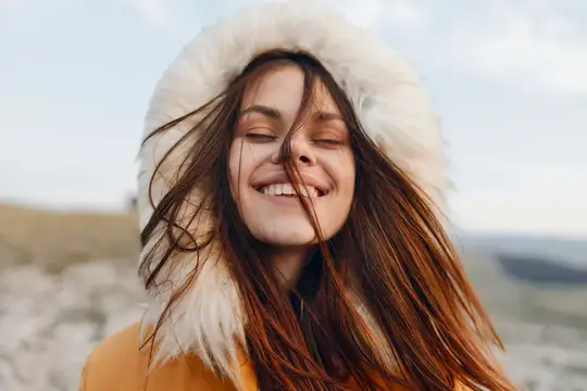 Улыбающаяся женщина в меховом пальто наслаждается горным видом