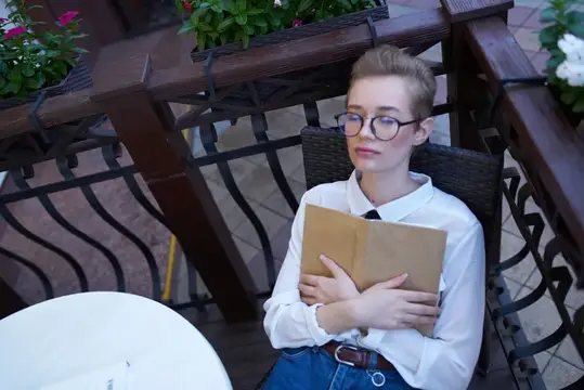 Студент с книгой в руках на открытом воздухе в летнем кафе, отдых и общение