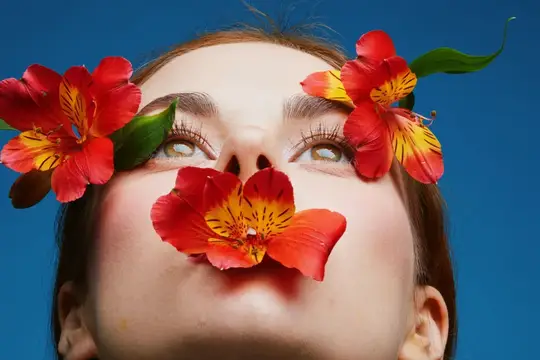 Портрет девушки с красными цветами на лице на синем фоне