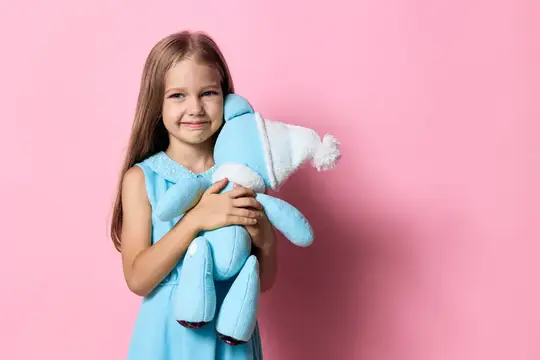 Улыбчивая девочка с длинными волосами обнимает голубого плюшевого мишку на розовом фоне