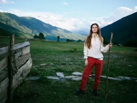 Молодая женщина с посохом стоит на горном лугу