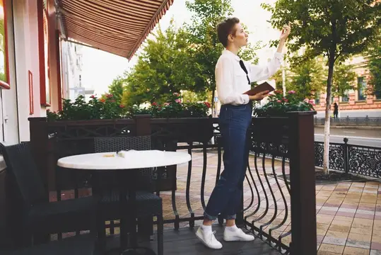 Девушка с книгой стоит на летней веранде кафе