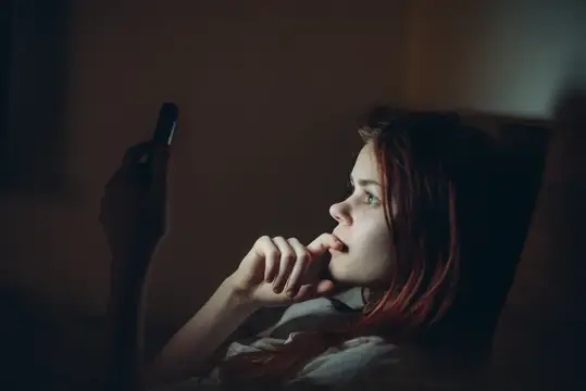 Рыжеволосая девушка смотрит на телефон в темноте