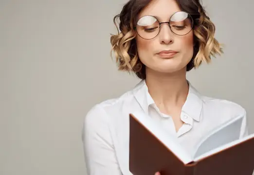 Молодая женщина в очках с закрытыми глазами читает книгу