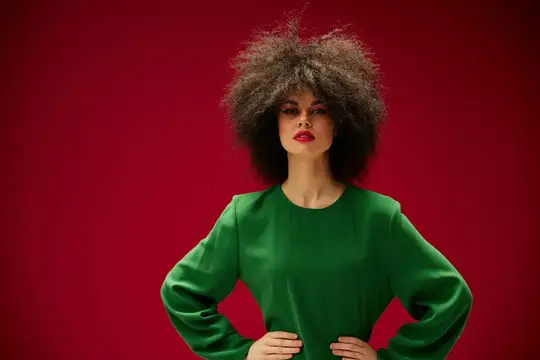 Стильная девушка с пышными кудрями в зеленом платье на красном фоне