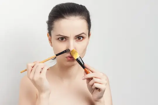 Девушка с кистями для макияжа у лица на сером фоне