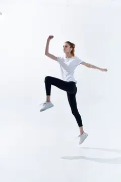 Молодая женщина в спортивной одежде прыгает на белом фоне