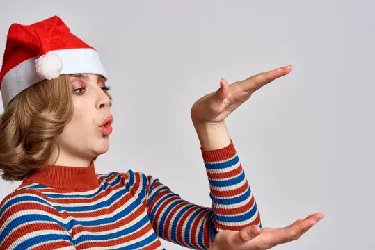 Молодая женщина в новогодней шапке сдувает с ладони блёстки